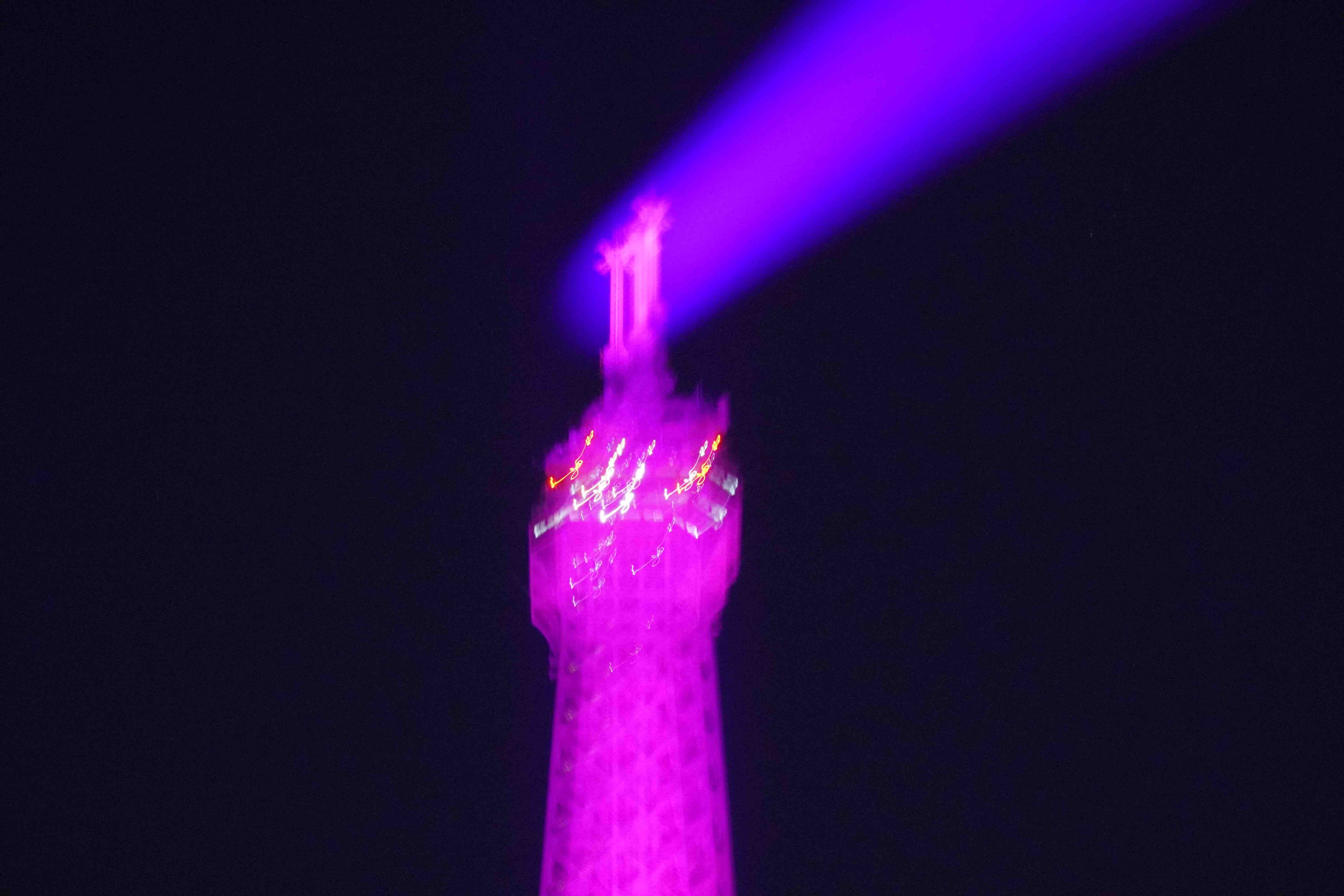 Out-of-focus top of Eiffel Tower in Paris, France lit with pink and purple lights.